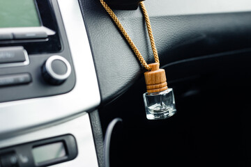 Small aroma glass jar car air freshener hanging on dashboard in vehicle saloon.
