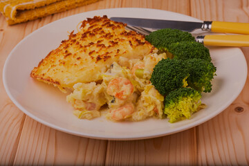 Seafood pie topped with mashed potato with some broccoli at the side on a white plate.