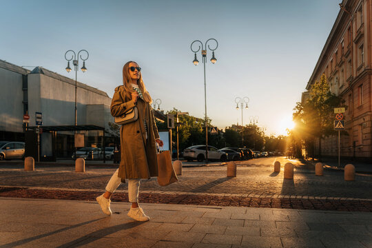 Woman walks along city street in evening after shopping with paper bag