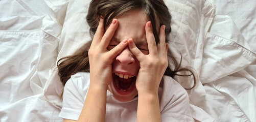 Portrait of little girl crying and screaming in horror on bed