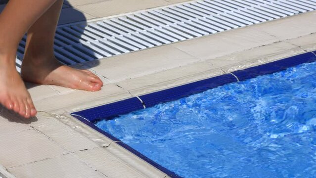 Close-up of a child's feet standing on the corner of the pool, checking the temperature of the water. Child gently probes the water in the pool before climbing into the water