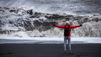 Fearless strong woman with outstretched arms faces powerful waves on black beach; concept of strong...