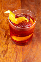 Negroni Cocktail in crystal glass with ice cubes and orange slice on wooden table