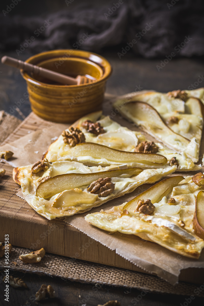 Wall mural Tarte flambee witgh pear, goat cheese, honey and walnuts on dark rustic wooden background, vertical