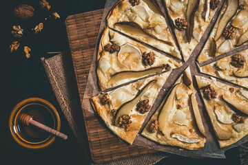 Tarte flambee witgh pear, goat cheese, honey and walnuts on dark rustic wooden background, top view