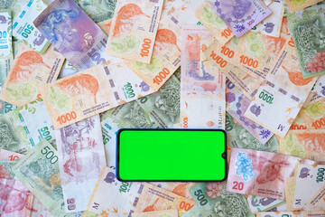 Mobile phone with green display on lots of currency notes of Argentine peso cash.Template,copyspace.Economic,financial crisis in Argentina, economy, money, bank concept.