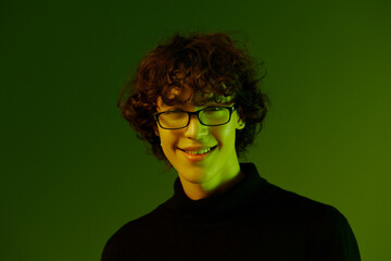 Man young man portrait close-up portrait in glasses fashion smile, hipster lifestyle, portrait green background mixed neon light, copy space