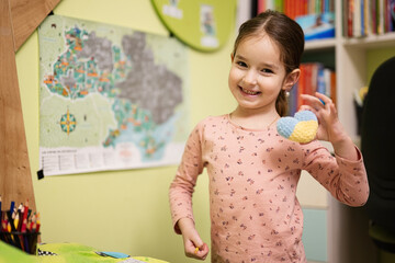 Cute little girl show heart Ukraine flag in her room.  Support ukrainian.