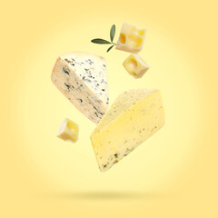 Pieces of different delicious cheese and leaves falling on yellow background