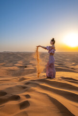 Fototapeta na wymiar A woman dressed like a princess in a desert during sunset. Dubai, UAE.