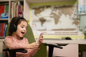Little girl wear headphones watching cartoons or kid video on her phone.