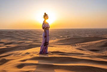 A woman dressed like a princess in a desert during sunset. Dubai, UAE. - obrazy, fototapety, plakaty