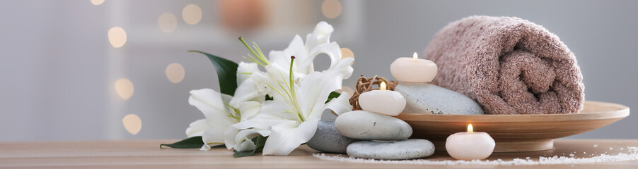 Fototapeta na wymiar Candles, hot stones, towel and flowers on table in spa cabinet, closeup. Banner design with space for text