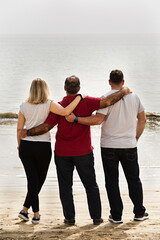 Padre y sus dos hijos abrazados mirando el mar.