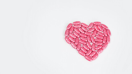 Pills of pink color in the form of a heart on a white background. Medicine, treatment, pharmacology, health. Top view Space for text on the left