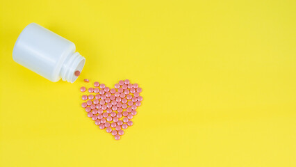 Vitamins in the form of a heart from a jar on a yellow background. Supplement with vitamins and...