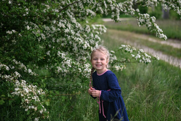 A girl with pigtails in nature in a blue dress near a flowering tree