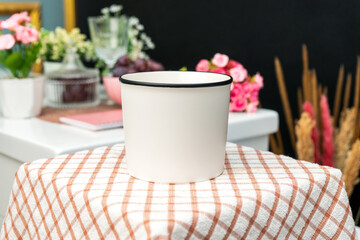 A white blank enamel mug on the top of a hand cloth with simple decorations arranged around it