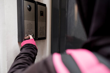 Unrecognizable bike courier ringing the bell on a flat door.