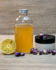 Natural homemade cosmetics set of face cream and face toner with half of lemon and wild rose flowers on the beige background.