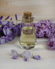Obraz na płótnie Canvas Composition of spa treatment with natural aromatic oil, lilac and wisteria flowers on white wooden background. 