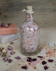 Homemade pink bath salt with Epsom and Himalayan salt, essential oils and wild rose petals. Natural soaps and crystals on blurred beige background.