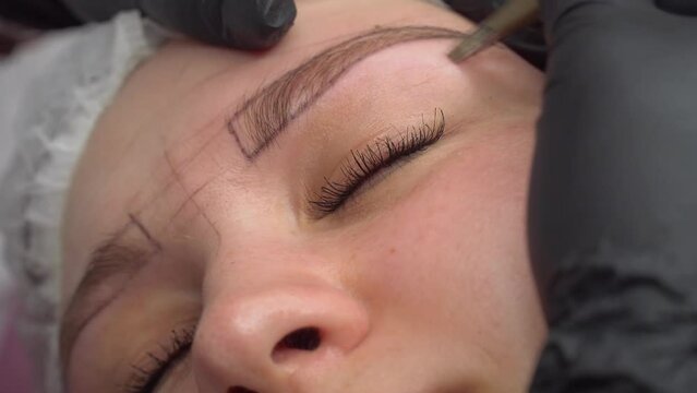 Makeup artist plucks eyebrows and doing eyebrow permanent makeup correction in a beauty salon. Concept makeup and cosmetology skin care.