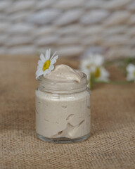                     Cosmetic cream with camomile flower for a eye, face and body on beige and white background.   