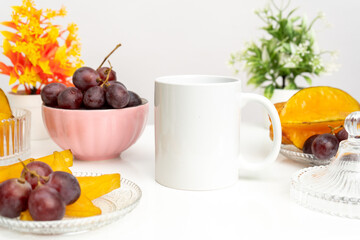 A white blank coffee mug on the top of a rounded mat with the fresh fruits arranged around it