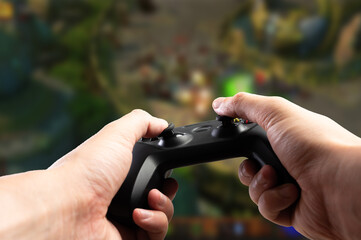 Fototapeta premium A gamer plays a video game with a gamepad in his hands against the backdrop of a video game on a large TV screen. Passion, game strategy, youth culture, virtual reality.