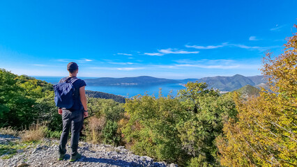Naklejka premium Man with scenic view from mountain summit of Vrmac Sveti Ilija on Kotor bay in summer, Adriatic Mediterranean Sea, Montenegro, Balkans, Europe. Fjord winding along coastal towns. Hiking Dinaric Alps