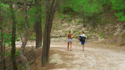 Obraz premium Young people (a man and a woman) walk along a picturesque forest mountain path to the 