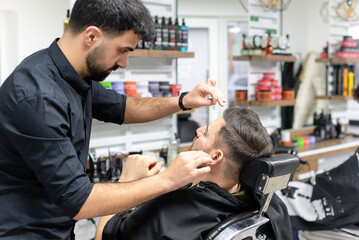 barber makes eyebrow correction for a man in the salon with a thread
