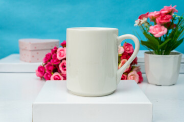 A white blank coffee mug standing out on top of a white box with some flower behind it