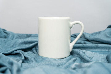 Fototapeta na wymiar A white blank coffee mug standing out on top of a blue cloth minimalist concept