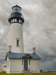 A tall white lighthouse with a small house against a sky with gray storm clouds. Mystical picture. Danger, storm, navigation, history, travel destinations, romance.