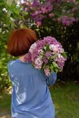 A red-haired girl in a spring park holds a bouquet of lilacs behind her back