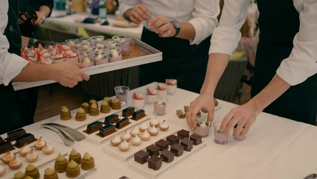 Three waiters arrange a variety of desserts on the white table in the buffet.