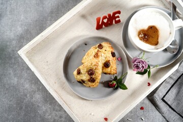 Valentines day breakfast  setting  - scones cappuccino heart and roses  on a tray, selective focus