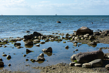 Big stones on a coast in the sea, with sailing ship on the horizon