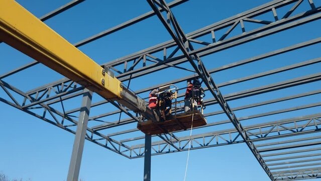 Metal frame constructiion site for a building. workers welding standing on cherry-picker