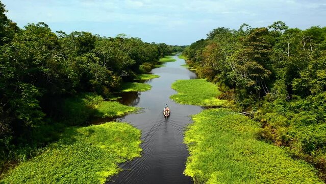 wide aerial shot of the amazon river with a boat in the middle crossing in the morning hours and peruvian jungle nature in the background