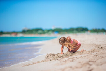 Little girl at tropical white beach making sand castle