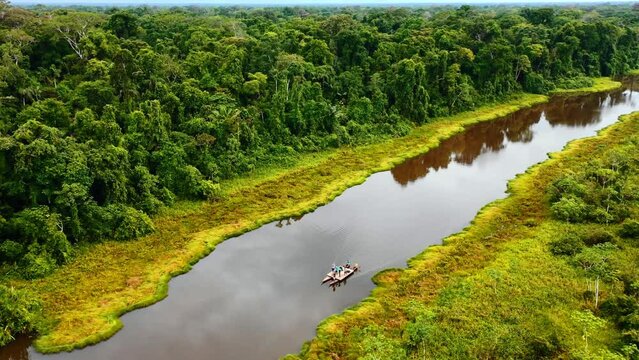 Close aerial shot of the amazon river with a boat in the middle crossing in the morning hours and peruvian jungle nature in the background