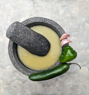 Stone mortar and pestle, green mexican sauce, garlic cloves, habanero and jalapeño chilies on cemet background