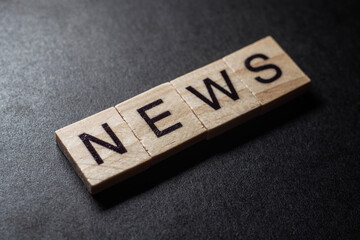 NEWS letter on wood block cubes on black background. Business communication concept.