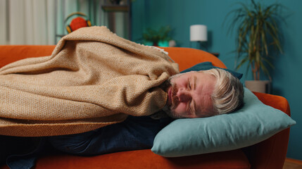 Tired middle-aged man lying down in bed taking a rest at home. Carefree mature senior gray-haired guy napping, falling asleep on comfortable sofa with pillows. Closed his eyes enjoy night nap alone