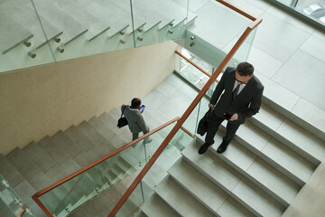 Above shot of two intercultural businessmen in formalwear using mobile phones while walking...