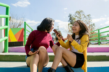 Amigas riendo sentadas en un parque. Chicas con celular