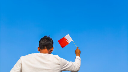 Boy holding Bahrain flag against clear blue sky. Man hand waving Bahraini flag view from back, copy space